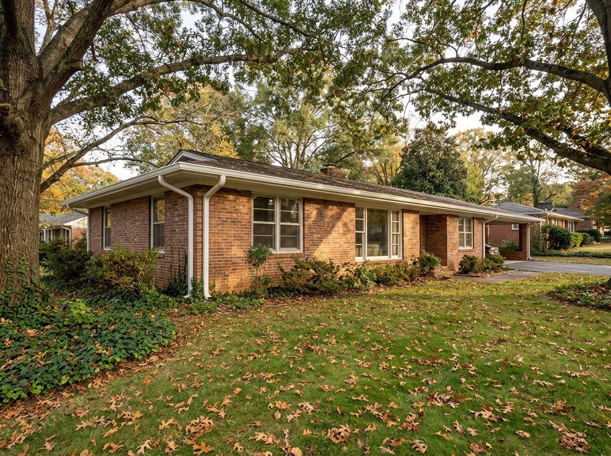 Brick ranch house with white gutters under big oaks, fall leaves on the lawn